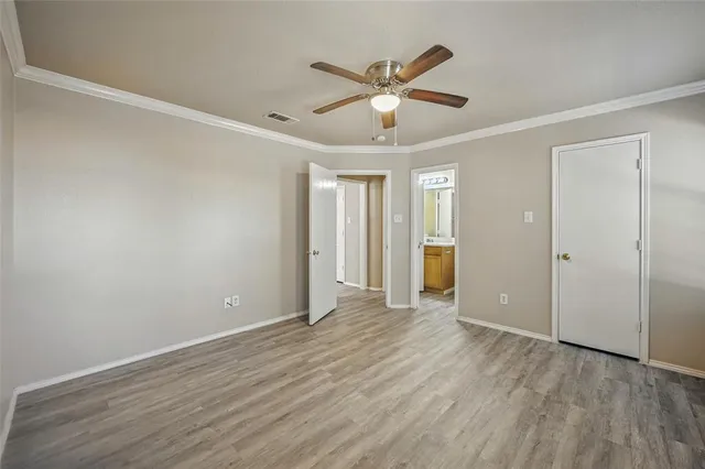 a view of an empty room with wooden floor and a ceiling fan