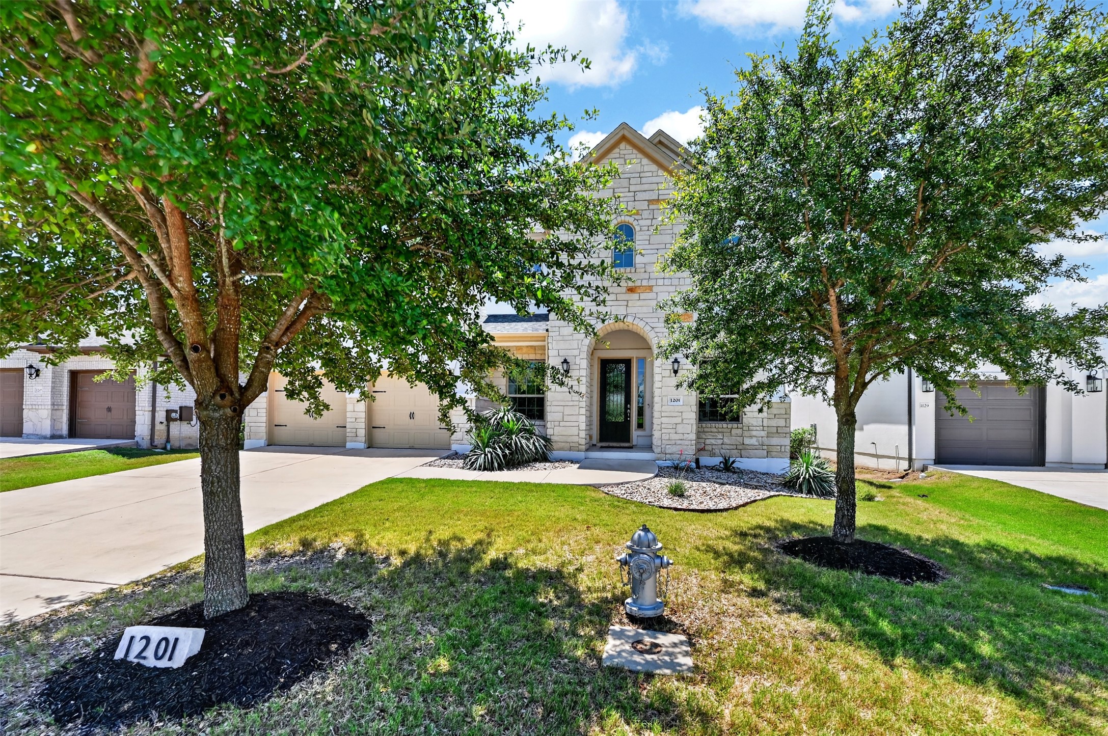1201 Positano Pass Leander, TX 78641 - Photo 2 of 40 Stone facade residence featuring a prominent arched entryway, mature front yard trees, and an attached two-car garage