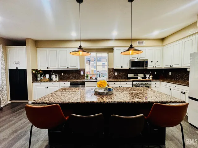 a kitchen with stainless steel appliances granite countertop a stove a refrigerator a sink a dining table and chairs with wooden floor