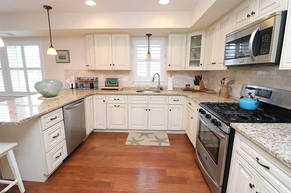 a kitchen with stainless steel appliances granite countertop a stove a sink dishwasher a refrigerator and white cabinets with wooden floor