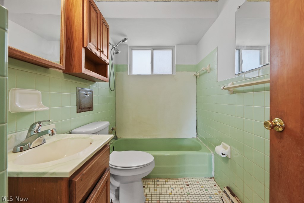 611 Herbert Road Akron, OH 44312 - Photo 22 of 30 Bathroom featuring a wood-finish vanity with an integrated sink, a built-in medicine cabinet, ceramic tile walls, a bathtub with shower, and a privacy window