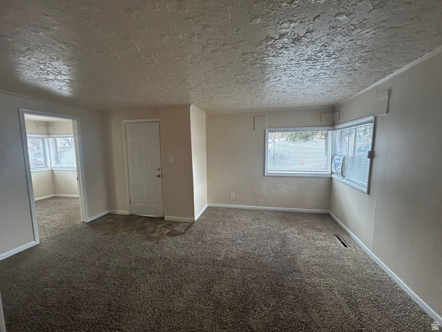 265 Rigdon Avenue, Unit 1 Salt Lake City, UT 84115 - Photo 3 of 15 Spacious living area featuring neutral-toned carpeting, ample natural light from multiple windows, textured ceiling, and a paneled entry door
