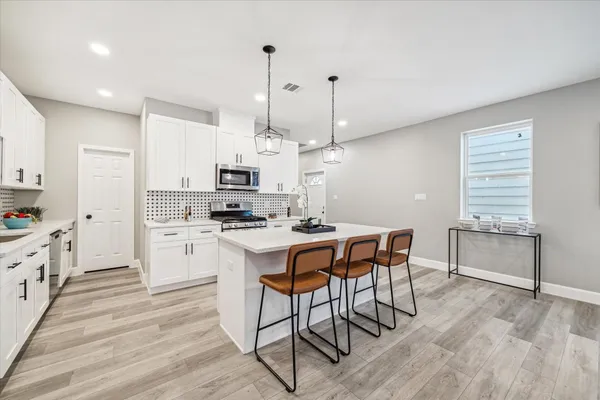 a kitchen with stainless steel appliances kitchen island granite countertop a stove a sink a refrigerator and white cabinets with wooden floor