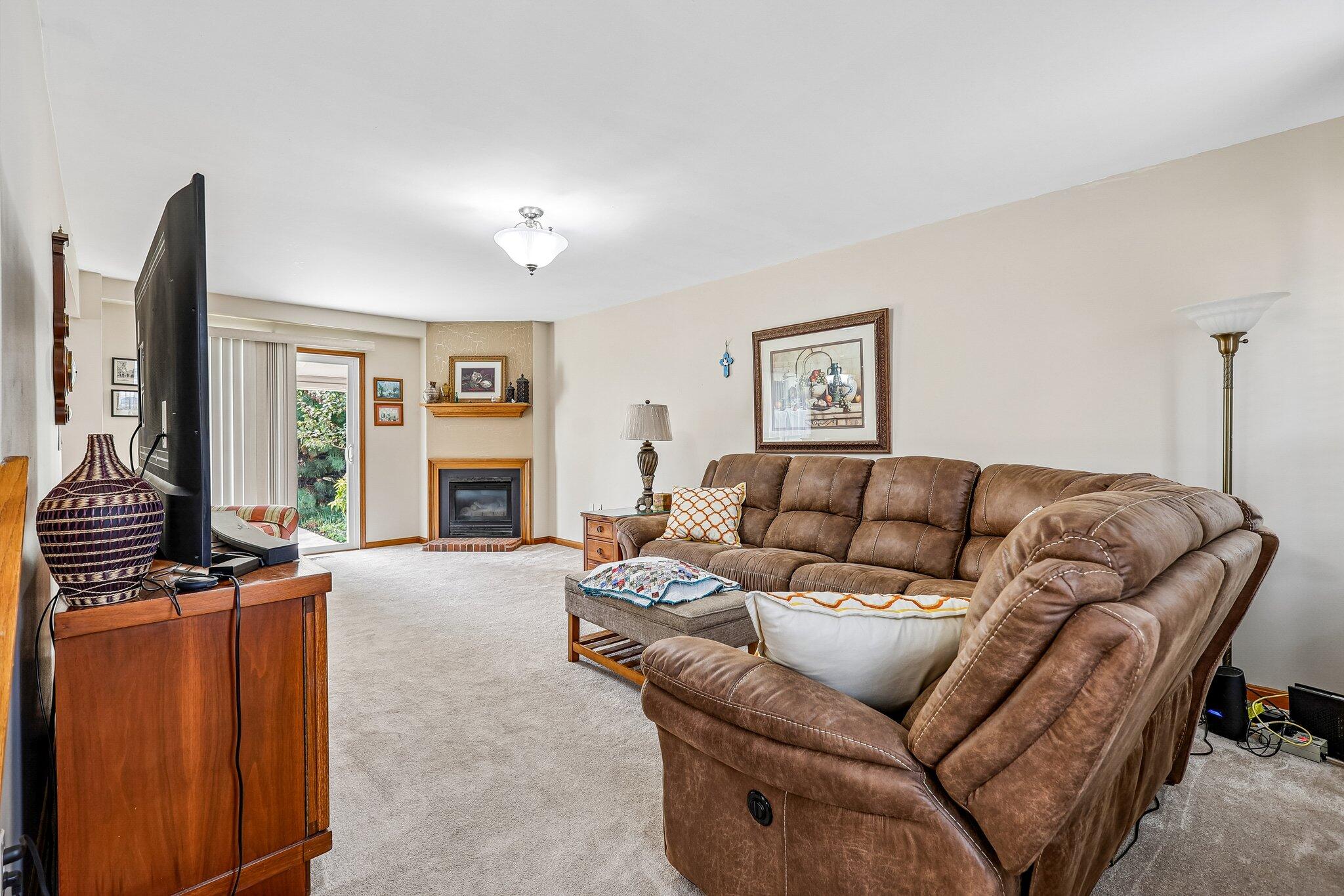 Corner fireplace with a wood mantle and brick surround, light neutral carpet, and sliding glass door