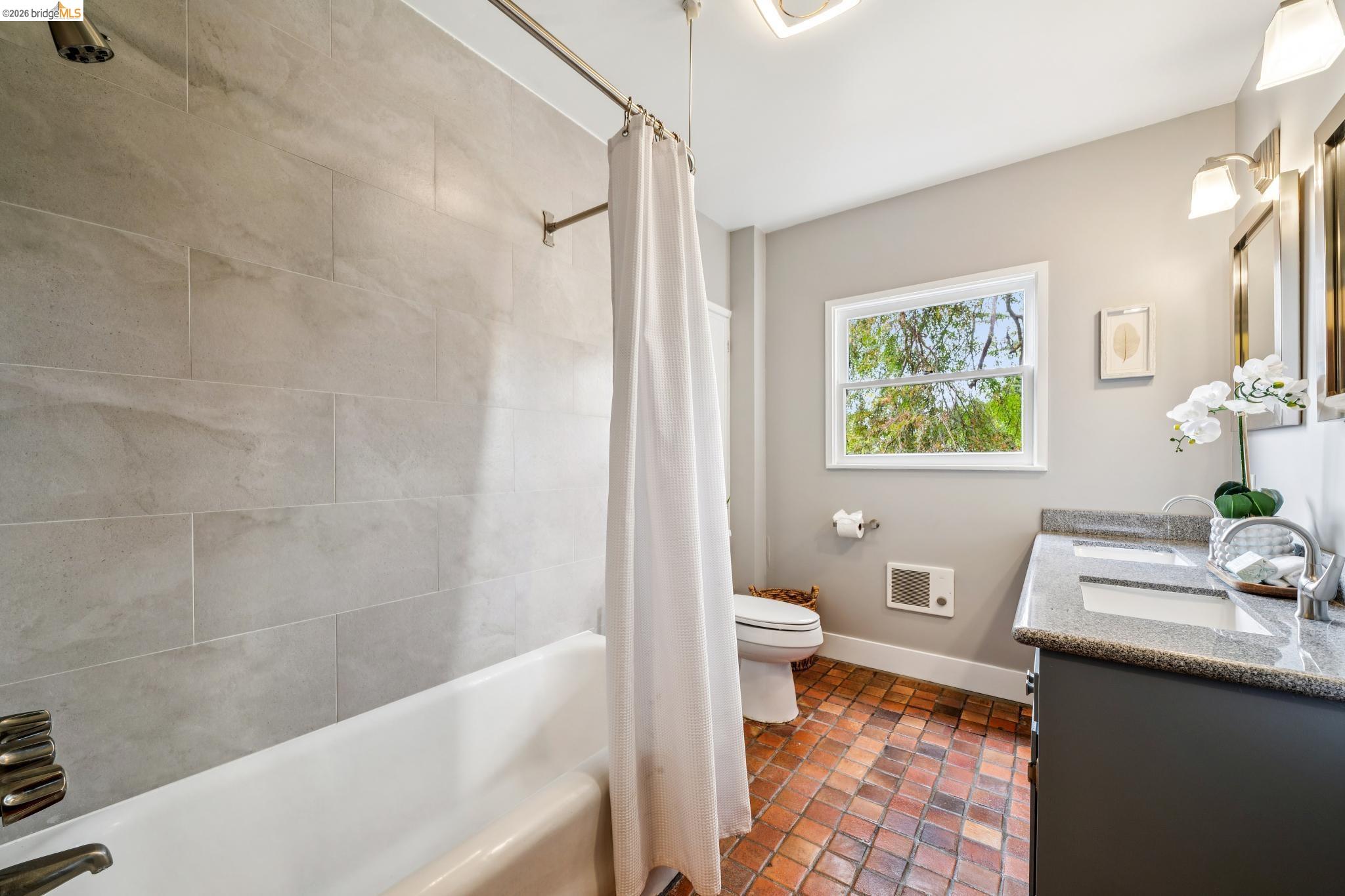 784 Cragmont Avenue Berkeley, CA 94708 - Photo 43 of 64 Bathroom featuring a dual-sink vanity with a stone-finish countertop, a white bathtub with a tiled surround, a window providing natural light, and square terra cotta flooring