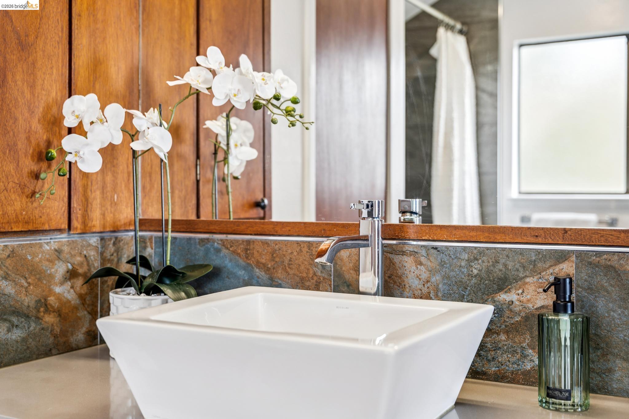 784 Cragmont Avenue Berkeley, CA 94708 - Photo 54 of 64 Modern vessel sink with a polished chrome faucet, set against a stone tile backsplash, wood-finish cabinetry, and a framed mirror