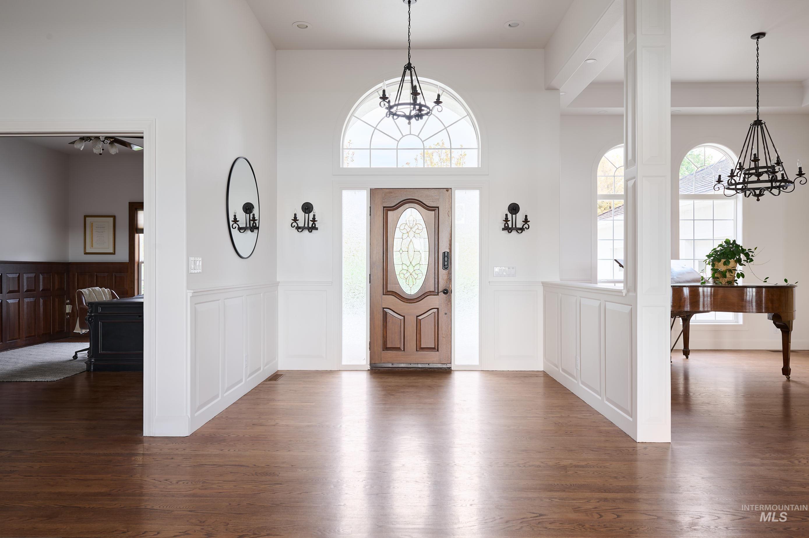 3931 North Triple Ridge Place Eagle, ID 83616 - Photo 5 of 45 Entryway with a chandelier, dark wood-type flooring, a wainscoted wall, a decorative wall, and a towering ceiling