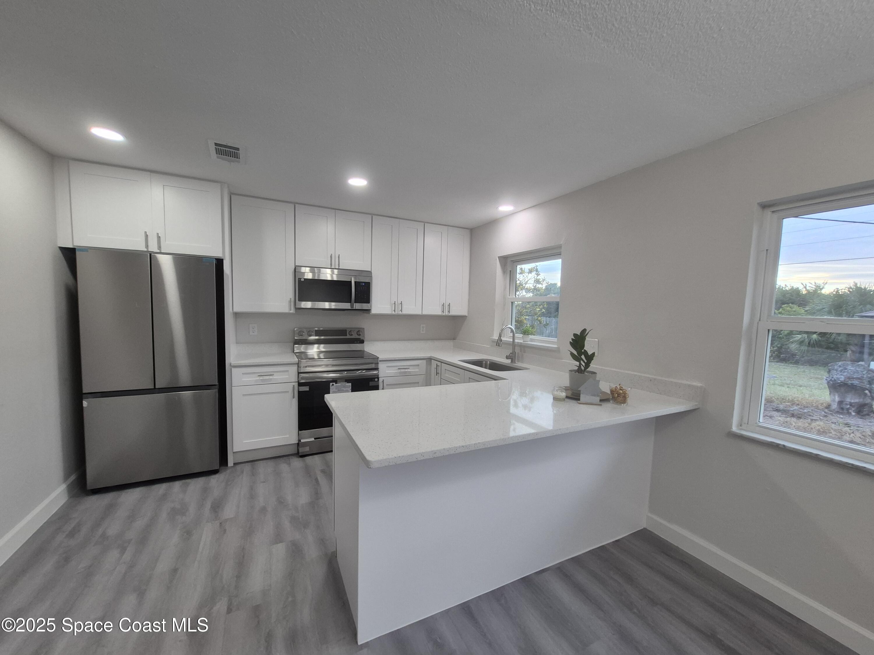 980 Bacon Circle Northeast Palm Bay, FL 32905 - Photo 16 of 50 a kitchen with a refrigerator a stove a sink and a oven with wooden floor