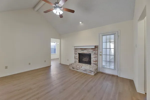 an empty room with wooden floor a fireplace a ceiling fan and windows