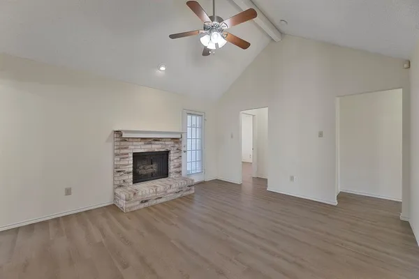 an empty room with wooden floor a chandelier fan and a fireplace
