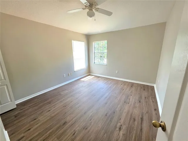 an empty room with wooden floor fan and windows