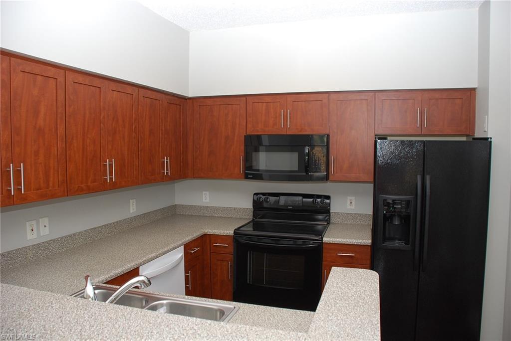 1130 Reserve Way, Unit 208 Naples, FL 34105 - Photo 5 of 14 a kitchen with stainless steel appliances wooden cabinets a stove and a microwave