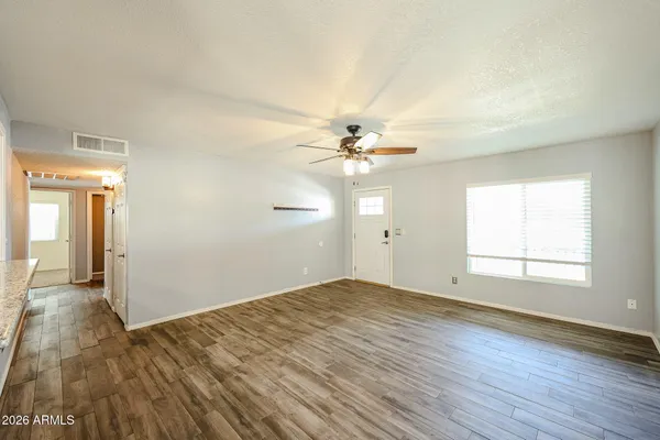 an empty room with wooden floor chandelier fan and windows