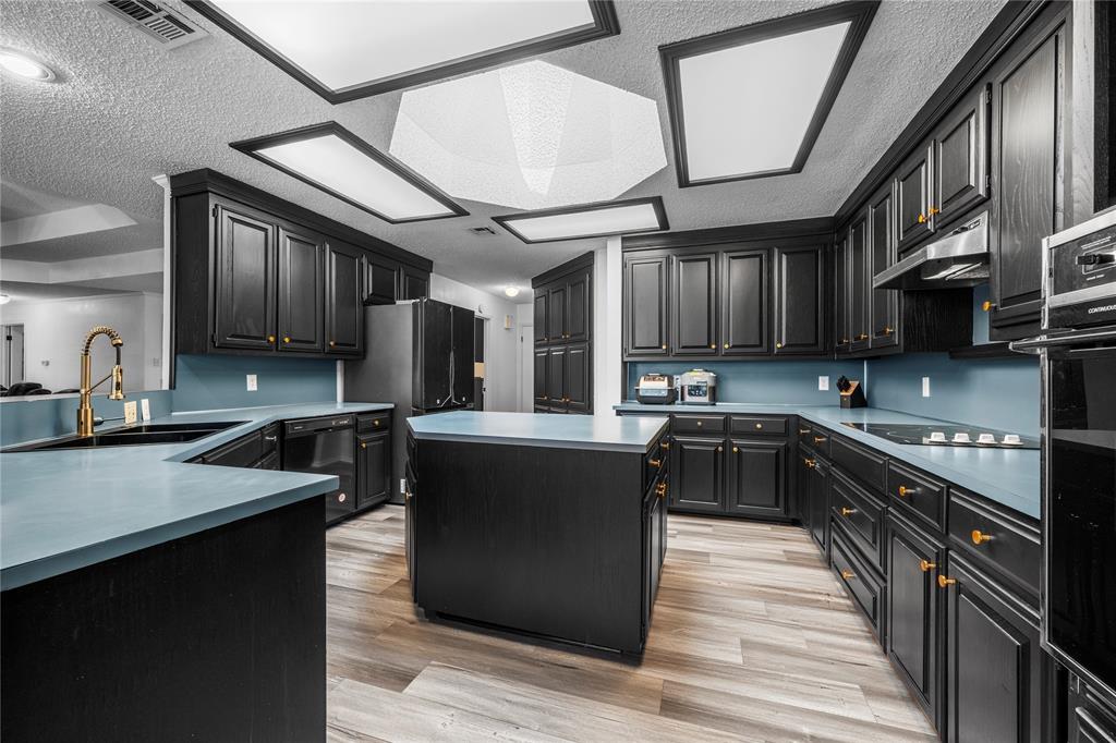 215 Lajuana Drive Waco, TX 76705 - Photo 11 of 33 Kitchen with a kitchen island, light wood finished floors, dark cabinetry, black appliances, and a textured ceiling