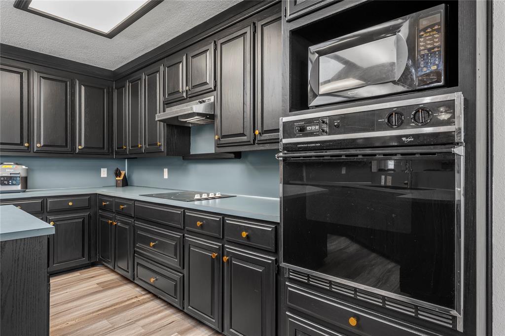 215 Lajuana Drive Waco, TX 76705 - Photo 14 of 33 Kitchen with black appliances, light wood-type flooring, light countertops, under cabinet range hood, and dark cabinets