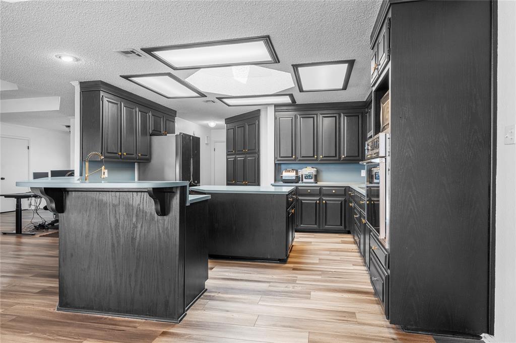 215 Lajuana Drive Waco, TX 76705 - Photo 15 of 33 Kitchen with a textured ceiling, light wood finished floors, a breakfast bar area, light countertops, and a kitchen island