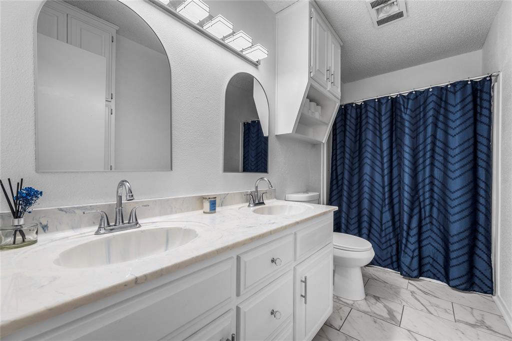 215 Lajuana Drive Waco, TX 76705 - Photo 24 of 33 Full bathroom featuring double vanity, a textured ceiling, light marble finish floors, curtained shower, and a textured wall