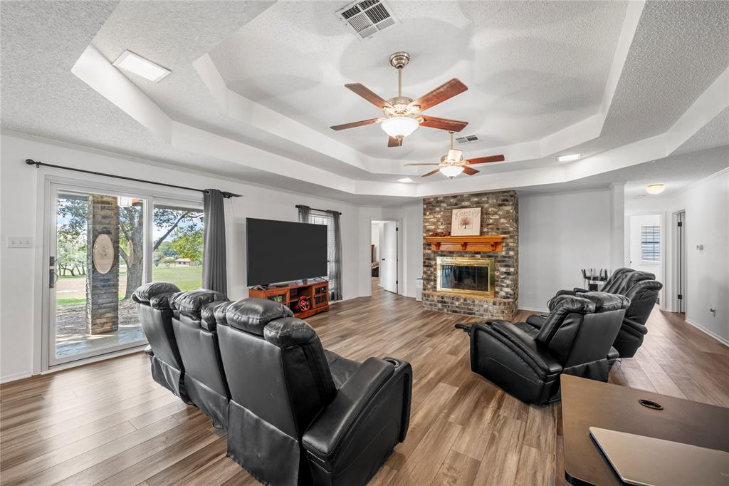 215 Lajuana Drive Waco, TX 76705 - Photo 5 of 33 Living room featuring wood finished floors, a textured ceiling, a fireplace, a raised ceiling, and a ceiling fan