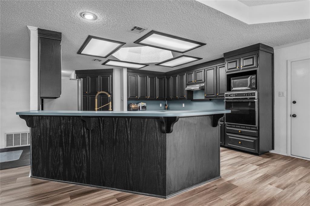 215 Lajuana Drive Waco, TX 76705 - Photo 10 of 33 Kitchen featuring a textured ceiling, a breakfast bar area, black oven, light wood-style flooring, and freestanding refrigerator