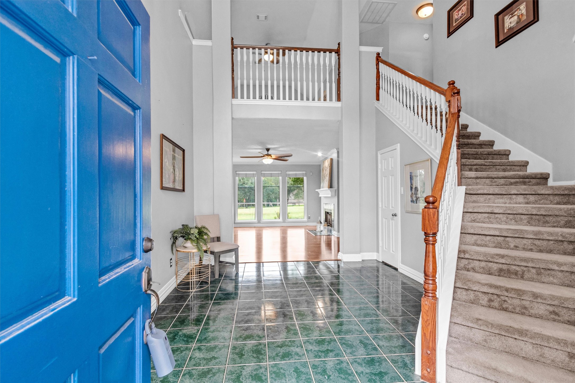 23 Alba Road Montgomery, TX 77356 - Photo 8 of 37 Bright and welcoming entryway featuring a striking blue door, high ceilings, and elegant tiled flooring. The staircase with wooden railing leads up to a second level, while large windows in the living area offer plenty of natural light and a view of the outdoors.