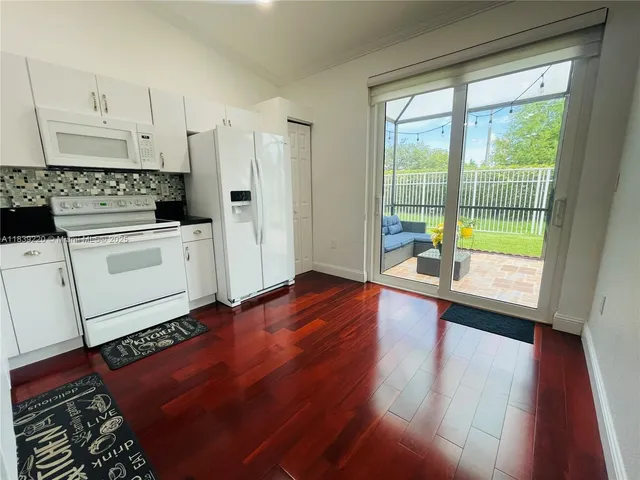 a open kitchen with granite countertop a stove top oven a sink and white cabinets with wooden floor