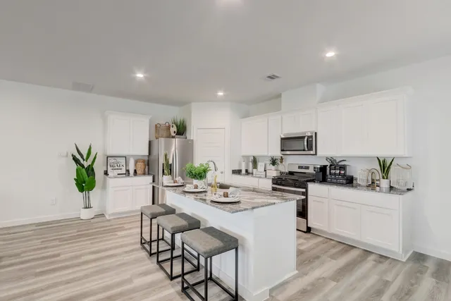 a kitchen with stainless steel appliances kitchen island granite countertop a sink a stove a dining table and chairs with wooden floor