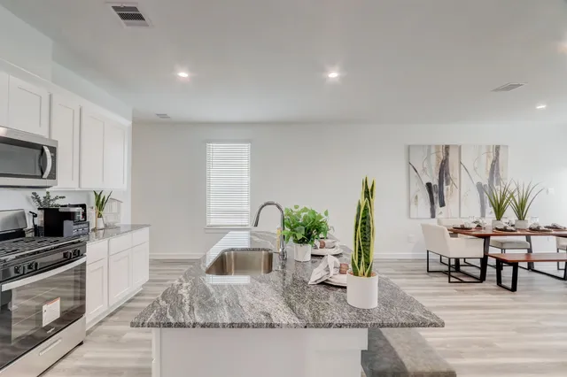 a kitchen with granite countertop a stove a sink a dining table and chairs