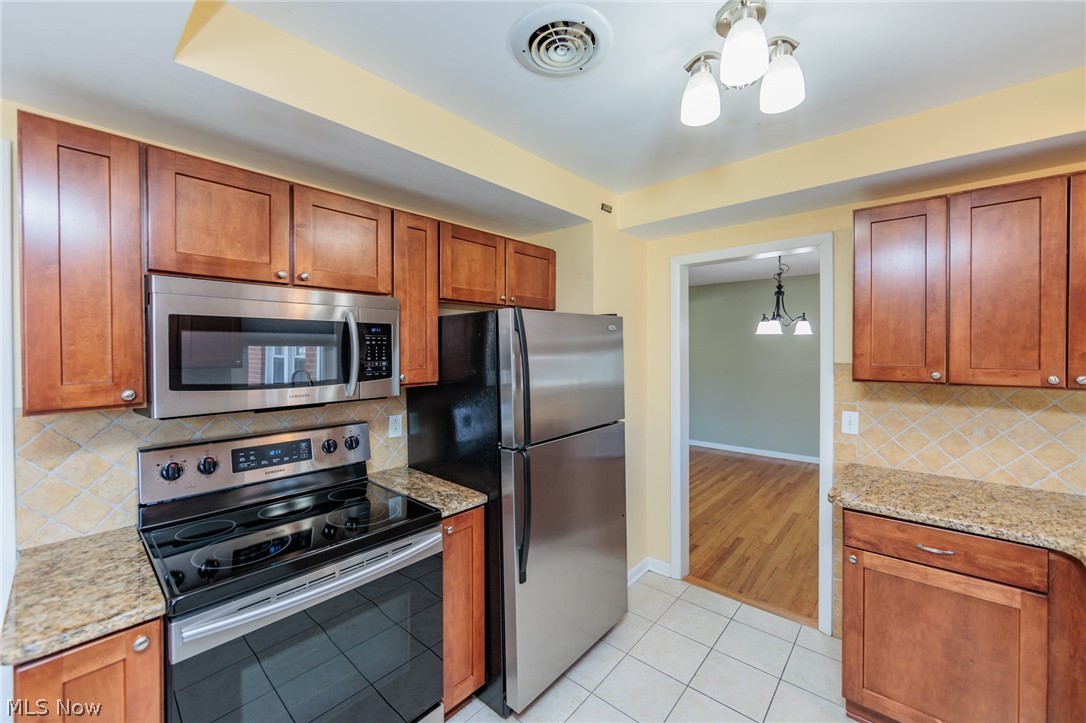 2444 Dysart Road Cleveland, OH 44118 - Photo 21 of 44 Kitchen with backsplash, light tile flooring, appliances with stainless steel finishes, a chandelier, and light stone counters
