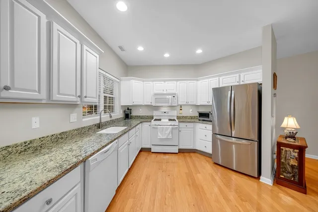 a white kitchen with granite countertop stainless steel appliances and wooden cabinets