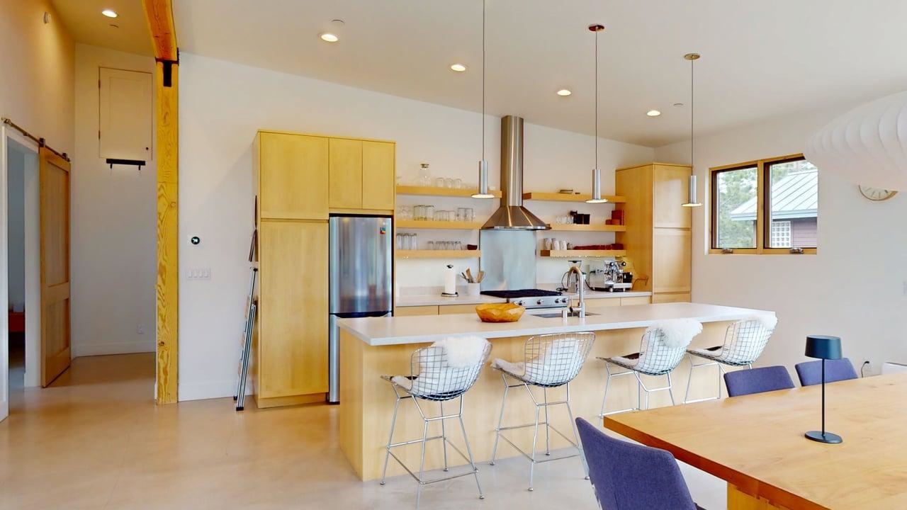 229 Ridgecrest Drive Mammoth Lakes, CA 93546 - Photo 16 of 74 Modern kitchen featuring light wood cabinetry, stainless steel appliances, a large center island with seating, open shelving, and a barn door entry