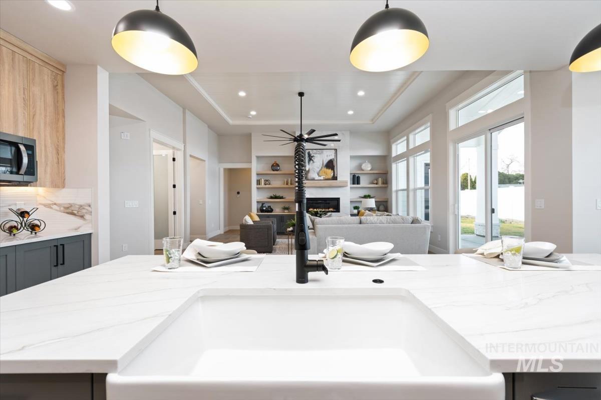 357 West Flour Mill Middleton, ID 83644 - Photo 15 of 49 Kitchen featuring light stone countertops, a tray ceiling, a warm lit fireplace, pendant lighting, and stainless steel microwave