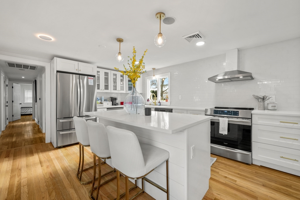 a kitchen with stainless steel appliances a stove a sink dishwasher a refrigerator and a dining table with wooden floor