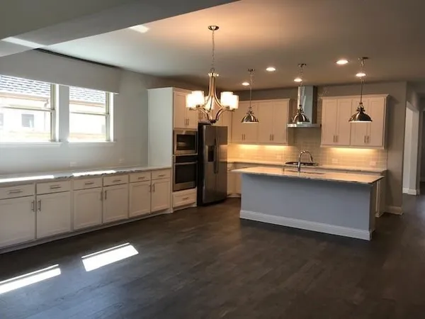 a large kitchen with kitchen island a stove a sink a refrigerator and white cabinets with wooden floor