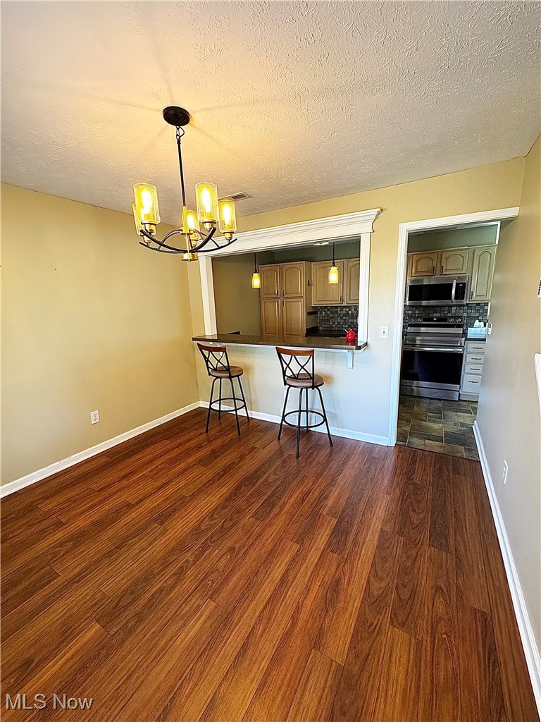 Kitchen featuring dark wood-type flooring, appliances with stainless steel finishes, a textured ceiling, a breakfast bar area, and a chandelier