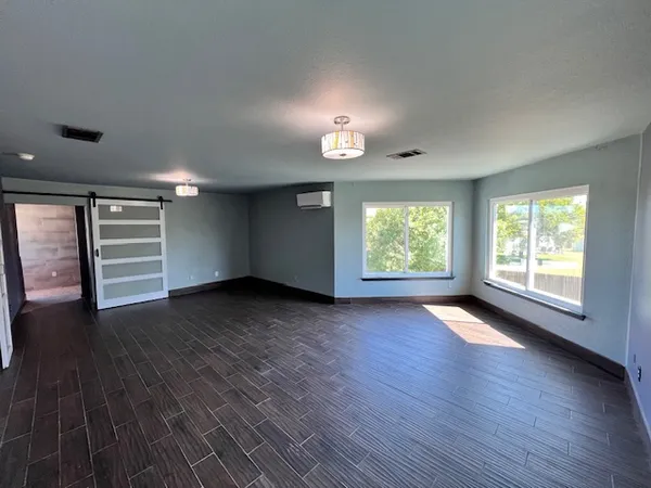 an empty room with wooden floor chandelier and windows
