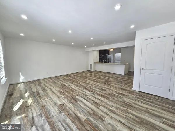 a view of an empty room with wooden floor and kitchen