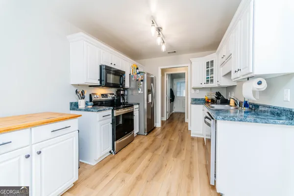 a kitchen with stainless steel appliances granite countertop a refrigerator a stove top oven a sink dishwasher and white cabinets with wooden floor