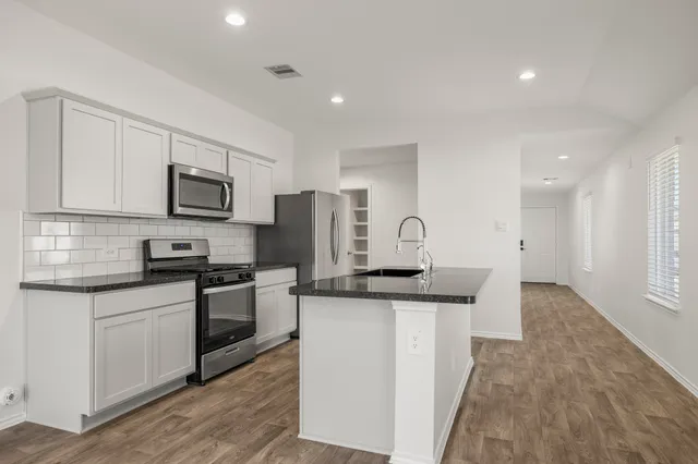 a kitchen with stainless steel appliances granite countertop a stove top oven a sink a refrigerator and white cabinets with wooden floor