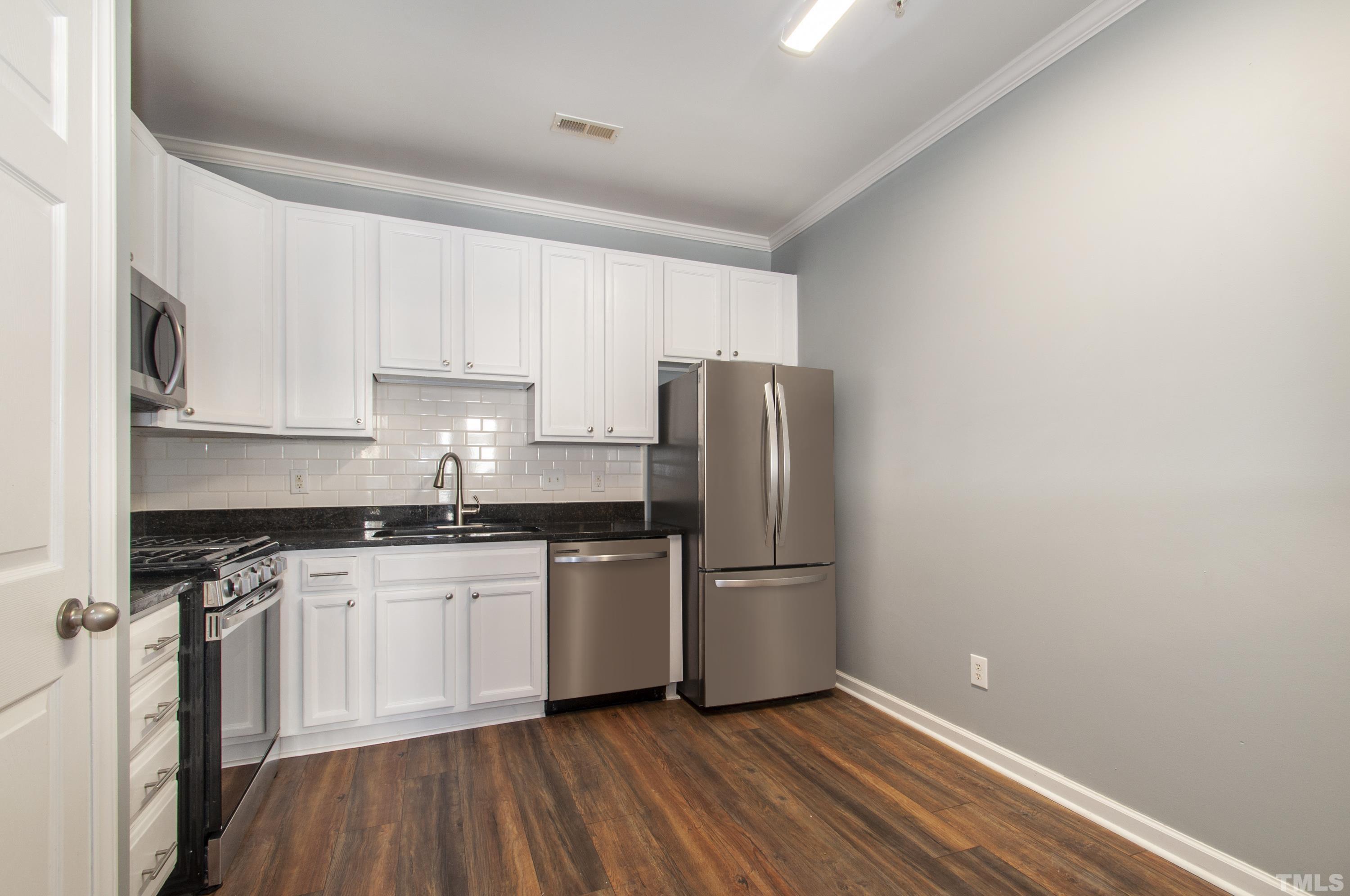 2210 Raven Road, Unit 102 Raleigh, NC 27614 - Photo 8 of 33 a kitchen with stainless steel appliances granite countertop a stove top oven a refrigerator and white cabinets with wooden floor