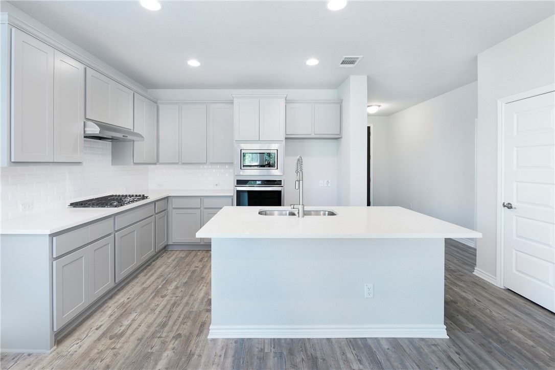 1613 Winding Stream Trail, Unit 75 Leander, TX 78641 - Photo 4 of 23 a kitchen with kitchen island a sink a stove a refrigerator and white cabinets