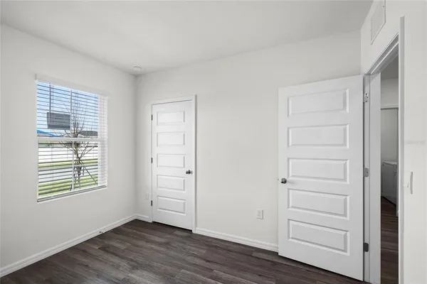 an empty room with wooden floor closet and windows