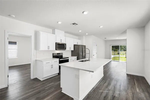 a kitchen with stainless steel appliances a stove top oven a refrigerator a sink and white cabinets with wooden floor