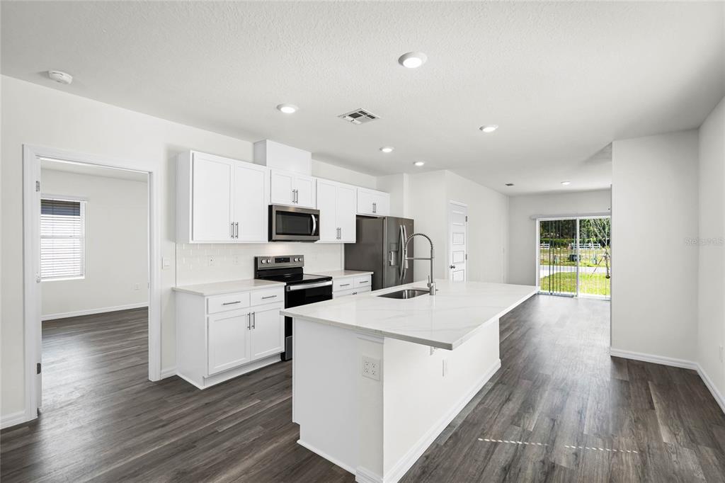 1726 Hummingbird Road Winter Haven, FL 33884 - Photo 4 of 28 a kitchen with stainless steel appliances a stove top oven a refrigerator a sink and white cabinets with wooden floor