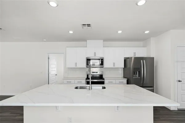 a kitchen with kitchen island a refrigerator a stove a microwave oven a sink and white cabinets with wooden floor