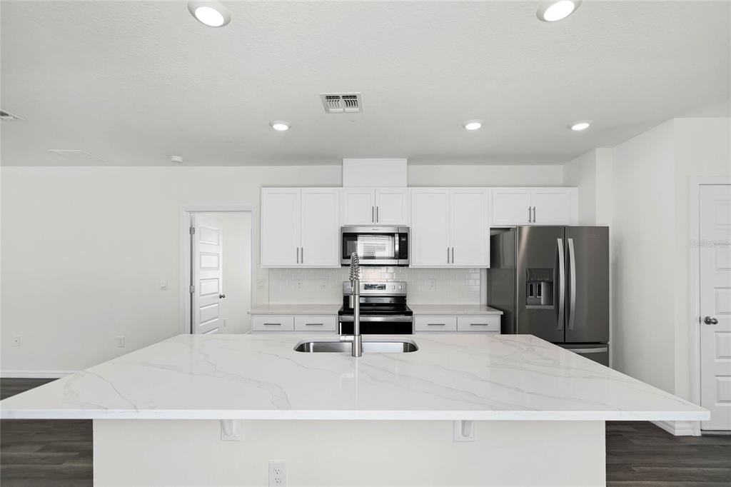 1726 Hummingbird Road Winter Haven, FL 33884 - Photo 6 of 28 a kitchen with kitchen island a refrigerator a stove a microwave oven a sink and white cabinets with wooden floor