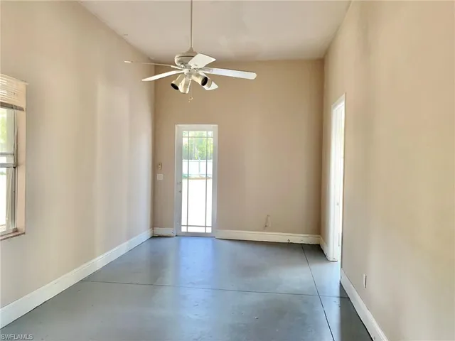 an empty room with chandelier fan and windows