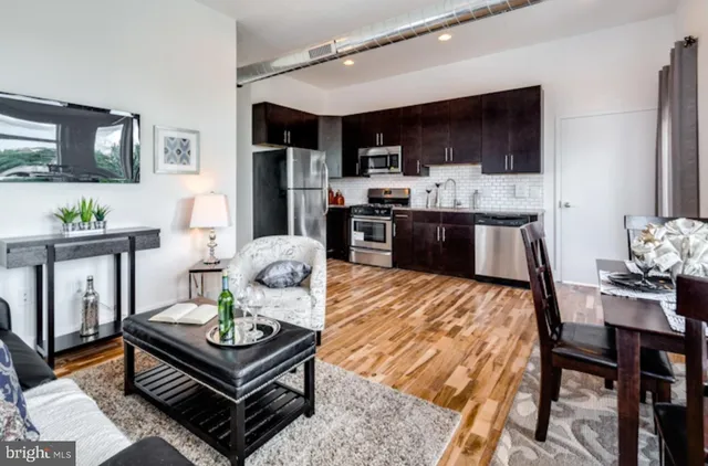 a living room with stainless steel appliances furniture a rug kitchen view and a kitchen island