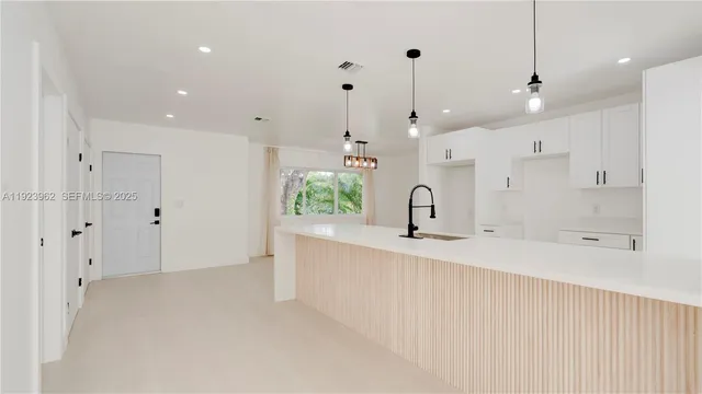 a large white kitchen with a sink a window and stainless steel appliances