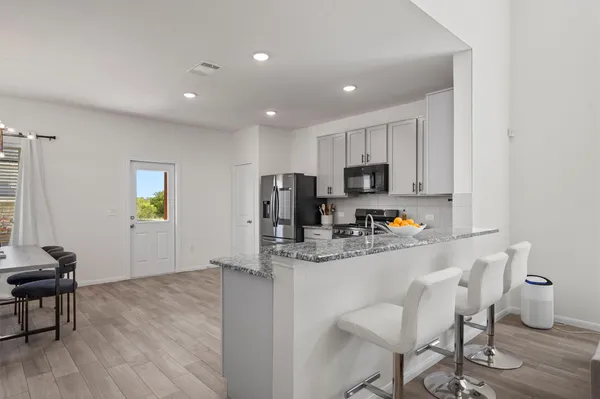 a kitchen with stainless steel appliances granite countertop a stove a sink a refrigerator white cabinets and wooden floor