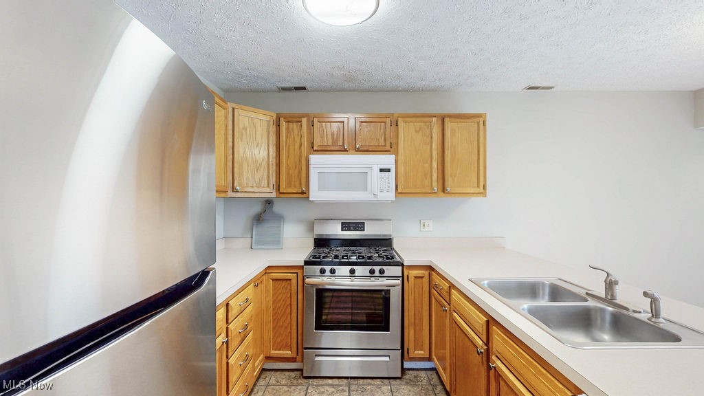 1426 Loop Road, Unit 1426 Kent, OH 44240 - Photo 12 of 40 Kitchen featuring appliances, light countertops, a textured ceiling, light tile patterned floors, and brown cabinetry